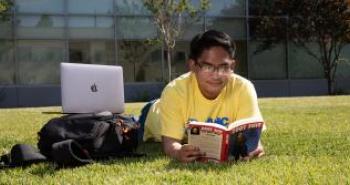 A male student lies in the lawn and reads book 
