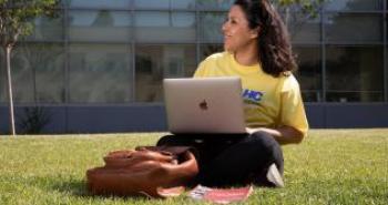 Female student sitting with laptop on the lawn.
